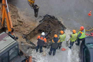 A group of road workers from public utilities in reflective special vests are discussing an emergency when digging a hole to eliminate the leakage of pipes in the middle of winter
