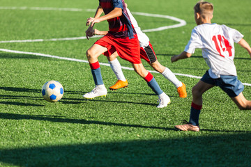 Boys in red white sportswear running on soccer field. Young footballers dribble and kick football ball in game. Training, active lifestyle, sport, children activity concept 