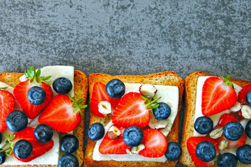 Healthy toasts with white cheese, fresh strawberries and blueberries. The concept of a healthy snack or lunch.