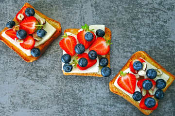 Healthy toasts with white cheese, fresh strawberries and blueberries. The concept of a healthy snack or lunch.