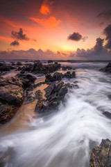 A scenery of sunrise with amazing unique rock formation and beautiful  flow of wave at Kemasik beach, Terangganu Malaysia. Soft focus during long exposure shot.