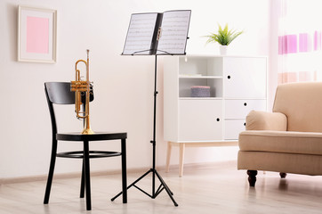 Trumpet, chair and note stand with music sheets in room