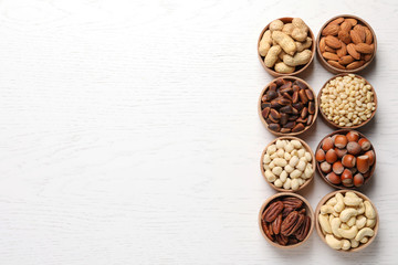 Bowls with different organic nuts and space for text on white wooden background, top view. Snack mix