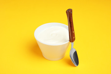 Bowl with creamy yogurt and spoon on color background