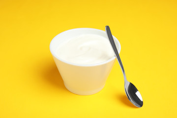 Bowl with creamy yogurt and spoon on color background