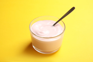 Glass bowl with creamy yogurt and spoon on color background