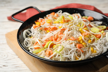 Frying pan with rice noodles, shrimps and vegetables on table
