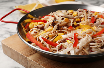 Frying pan with rice noodles, meat and vegetables on table