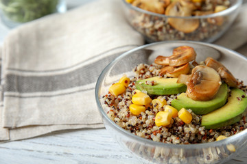 Healthy quinoa salad with vegetables in bowl on wooden table, closeup. Space for text