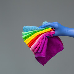 A hand in a rubber glove holds a set of colored microfiber cloths on a neutral background. The concept of bright spring, spring cleaning.