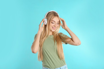 Beautiful young woman listening to music with headphones on color background