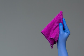 A hand in a rubber glove holds a bright microfiber duster on a neutral background. Сoncept of bright spring, spring cleaning.