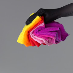 A hand in a rubber glove holds a set of colored microfiber cloths on a neutral background. The concept of bright spring, spring cleaning.