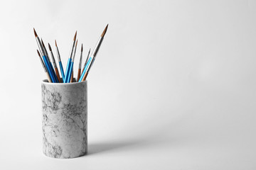 Holder with different paint brushes on white background. Space for text