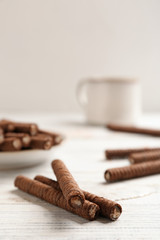 Delicious chocolate wafer rolls on white wooden table, space for text. Sweet food