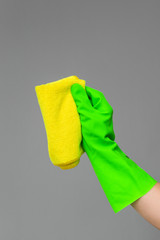 A hand in a rubber glove holds a bright microfiber duster on a neutral background. Сoncept of bright spring, spring cleaning.