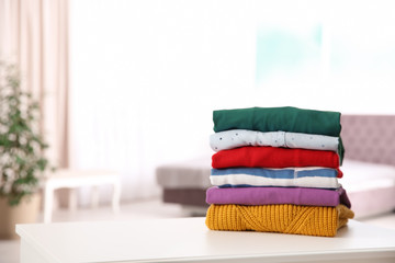 Stack of folded bright clothes on table against blurred background. Space for text