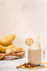 Tasty fresh drink in glass mug with plastic tube and slice of banana on napkin near fruits and bananas on chopping board on wood table 