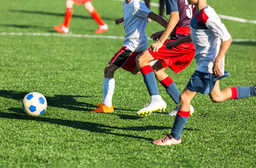 Boys in red white sportswear running on soccer field. Young footballers dribble and kick football ball in game. Training, active lifestyle, sport, children activity concept 