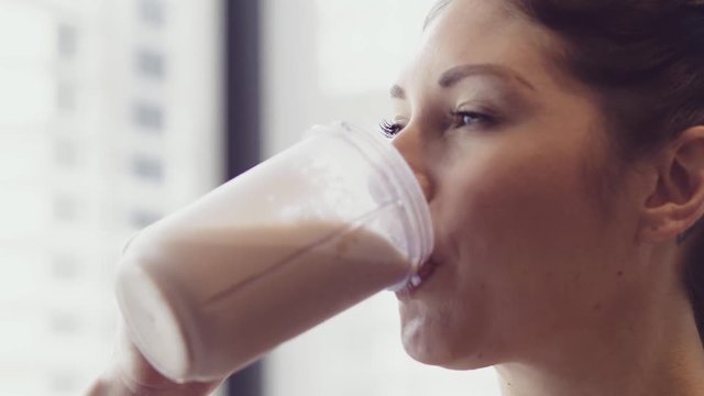 Close up of a happy blue-eyed brunette as she drinks a protein shake in a bright room