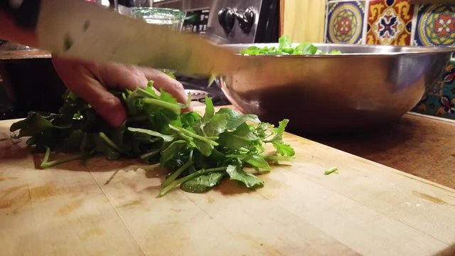 Closeup of a pile of freshly washed arugula and a chef&sbquo;&Auml;&ocirc;s knife chops it into bit size pieces.