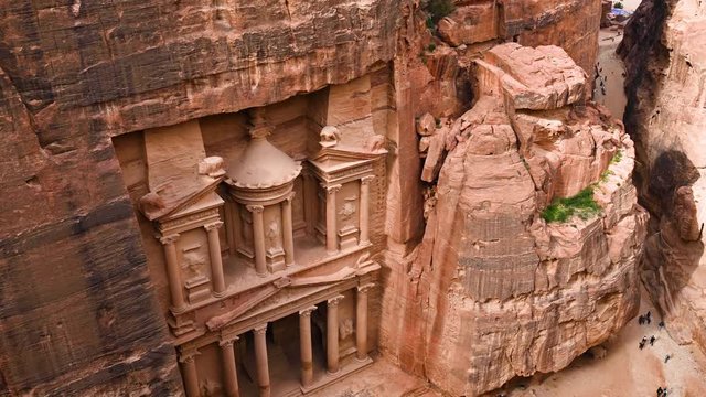 Aerial view of the beautiful Al Khazneh (The Treasury) with tourists admiring it from below. Petra is a historical and archaeological city in southern Jordan.
