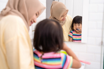 asian muslim mom brush her kid's teeth in the bathroom