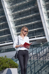 Fototapeta premium Happy blonde business woman in sunglasses with notebook against of modern building