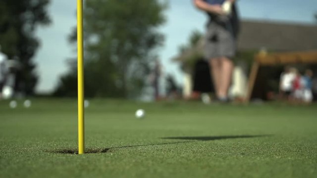 A golf ball rolls towards a hole with a flagstick.