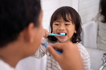 happy kid and dad having fun while brushing their teeth together in the bathroom sink