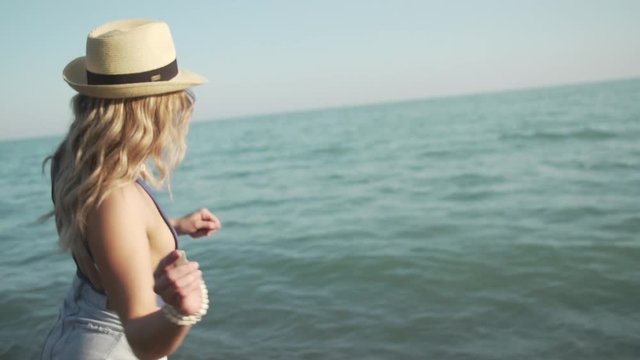 A blonde girl skips a rock in slow motion along the calm water at sunset.