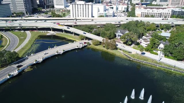 Drone clip tilts up to reveal Downtown Orlando over small pond.