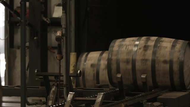 Bourbon barrels moving down a conveyor belt inside of a factory.