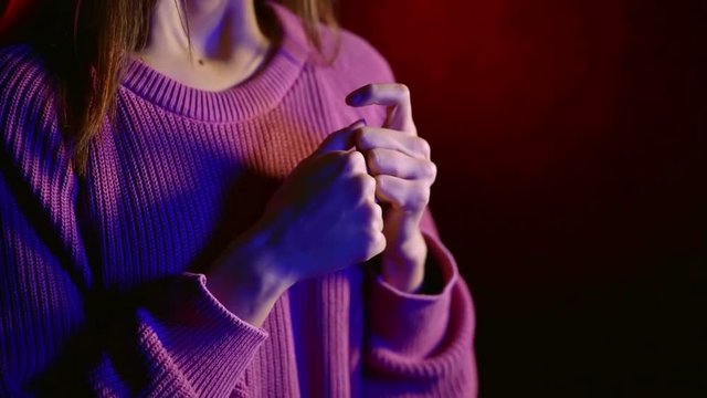 nervous young woman is kneading her hands, touching fingers in dark room with soffits