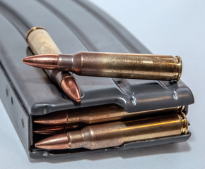 A rifle magazine loaded with 223 caliber bullets with two separate bullets on top of it on a white background