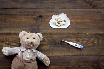 Childhood diseases concept. Treatment of children.Teddy bear toy, thermometer and pills on dark wooden background top view copy space
