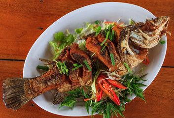 Whole fried fish spicy served with sliced fresh chili peppers, green onions and basil served in a restaurant in Krabi, Thailand