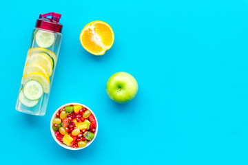 Diet rich in fruits. Slimming diet. Fruit salad near fruit lemon and cucumber water on blue background top view space for text