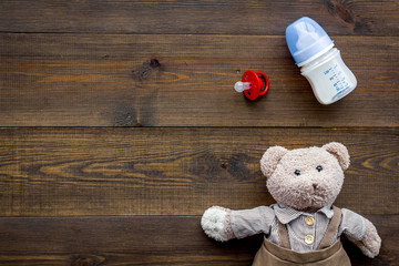 Feed baby concept. Teddy bear toy near small bottle with food on dark wooden background top view space for text