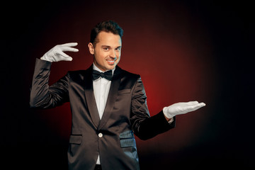 Professional Occupation. Showman in suit and gloves standing isolated on wall showing trick looking camera playful