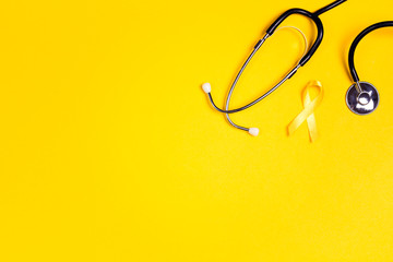 Childhood Cancer Awareness Yellow Ribbon and stethoscope on yellow background with copy space.