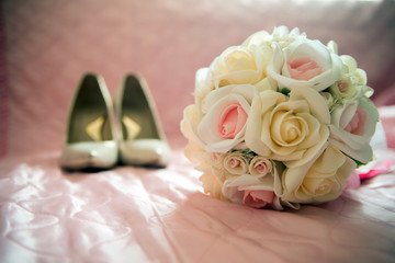 Bridal bouquet of white roses, on a pink bed, short focus, shoes in the background
