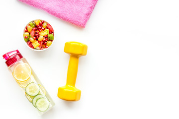 Fototapeta na wymiar Healthy lifestyle, healthy habits. Detox water, fruit salad, sport equipment dumbbells on white background top view space for text
