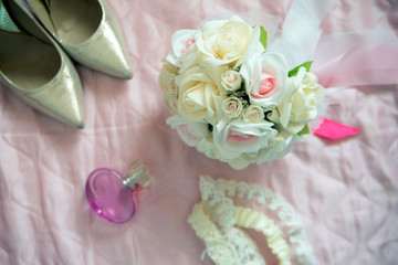 Bridal bouquet of white roses, on a pink bed, short focus, shoes, perfume and lace in the background