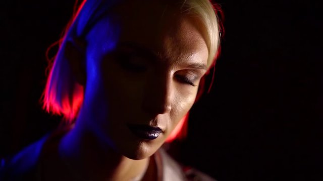young androgynous model with female makeup is rising eyes and viewing camera, in black background