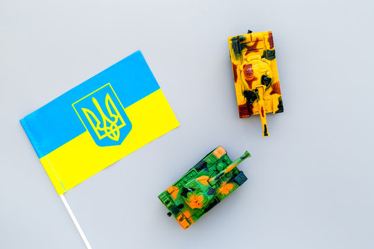 War, military threat, military power concept. Ukraine. Tanks toy near Ukrainian flag on grey background top view