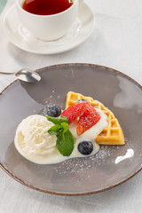 Fresh belgian waffles with ice cream and berries and cup of tea served on the table