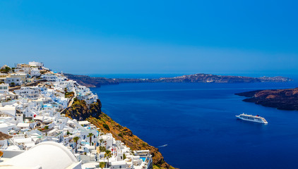 View of Santorini volcanic landscape with small white buildings, sea with a sailing ship and cliffs...