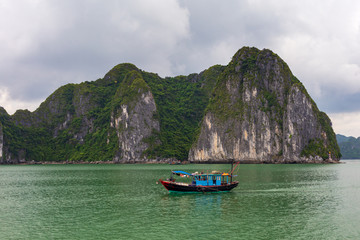 Naklejka na ściany i meble Halong bay rock formations with a Vietnamese traditional blue fishing boat, UNESCO world natural heritage, Vietnam.