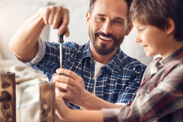 Father and little son at home standing dad screwing screw laughing happy looking at boy holding chair leg close-up